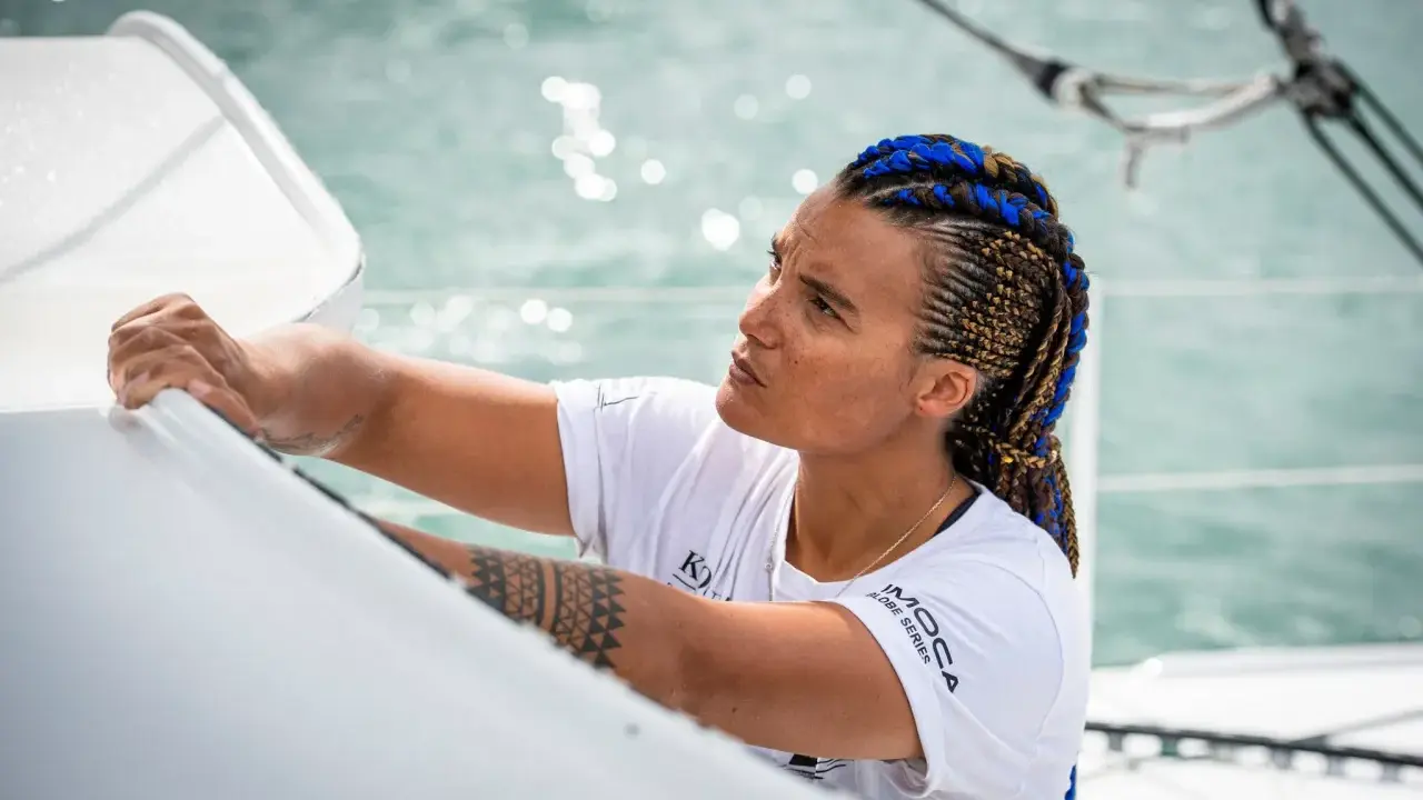 Marie Tabarly, concentrée, ajuste une voile sur son bateau. Ses tresses bleues et brunes flottent au vent.