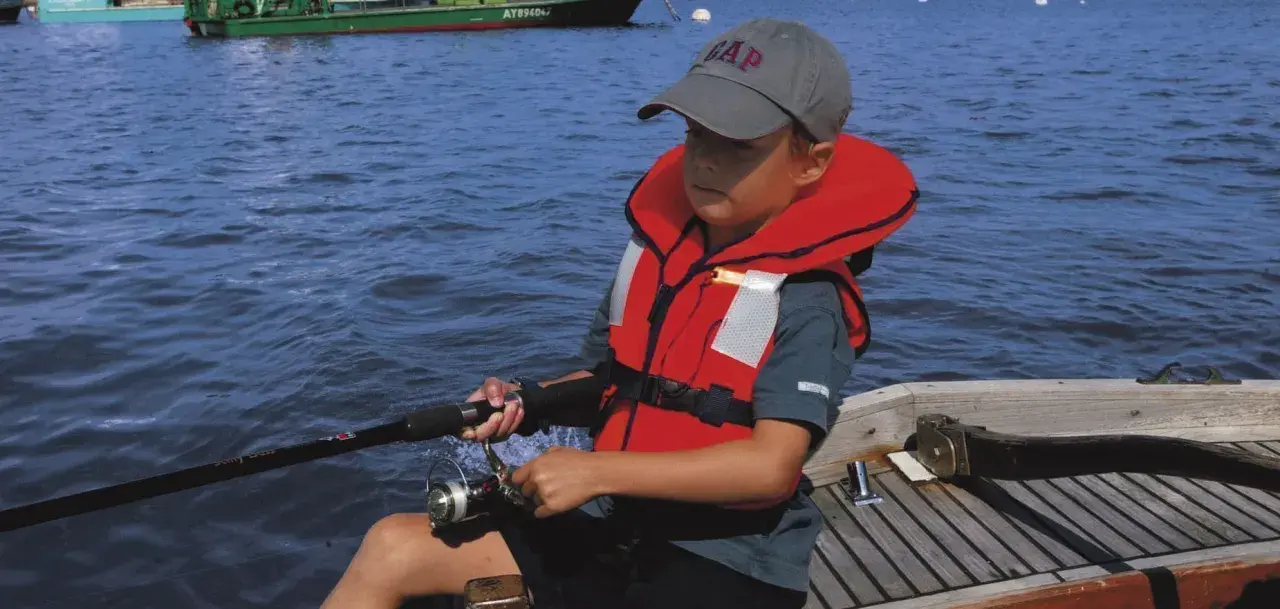 Un enfant pêche en mer, portant un gilet de sauvetage obligatoire. La question du gilet de sauvetage obligatoire jusqu'à quel âge est cruciale pour la sécurité nautique.