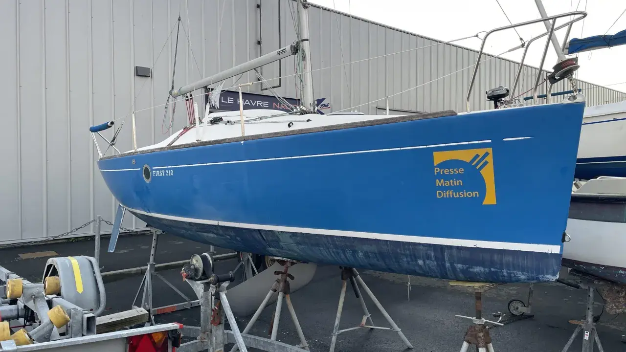 Voilier bleu FIRST 210 sur bers, prêt pour la saison. Le logo "Presse Matin Diffusion" est visible sur la coque.