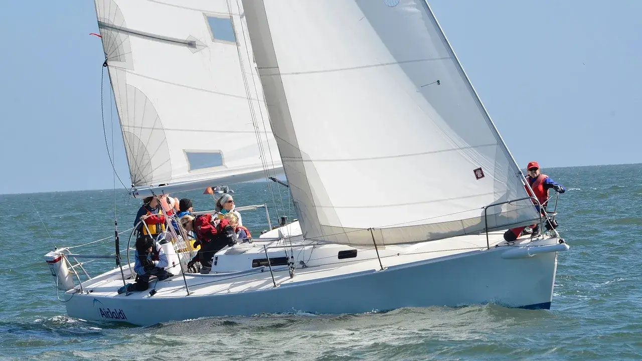 Équipage concentré sur un foc voilier blanc, naviguant sur une mer agitée sous un ciel bleu clair.