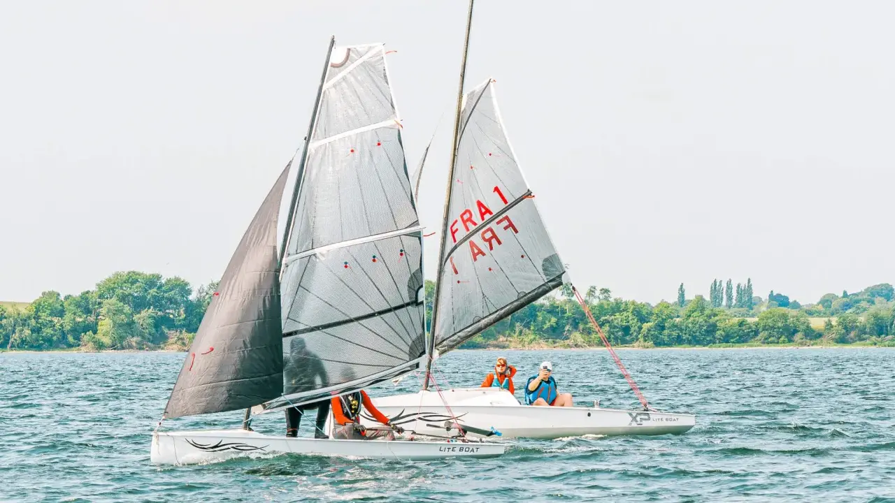 Deux voiliers d'aviron modernes naviguent sur un lac, avec des équipages concentrés sur la course.