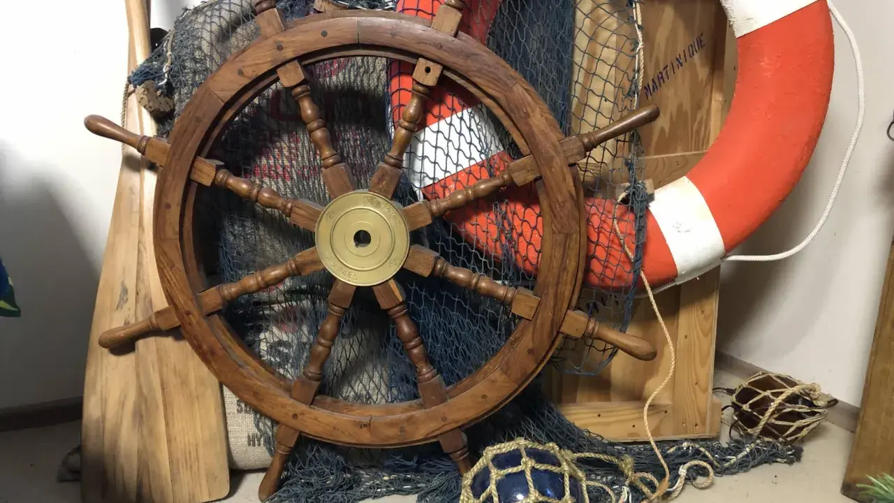 Roue de gouvernail en bois, filet de pêche, bouée de sauvetage orange et pagaies évoquent un safran de bateau prêt pour l'aventure.