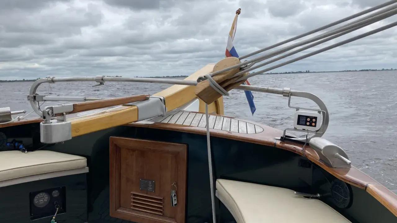 Installation pilote automatique barre franche sur un voilier, avec drapeau néerlandais et ciel couvert.