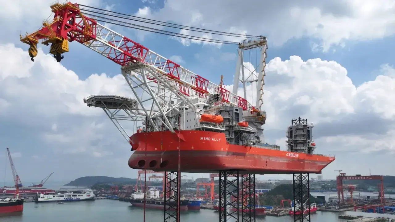 Le bateau grue "Wind Ally" est prêt à installer une éolienne en mer. Sa structure imposante domine le port.