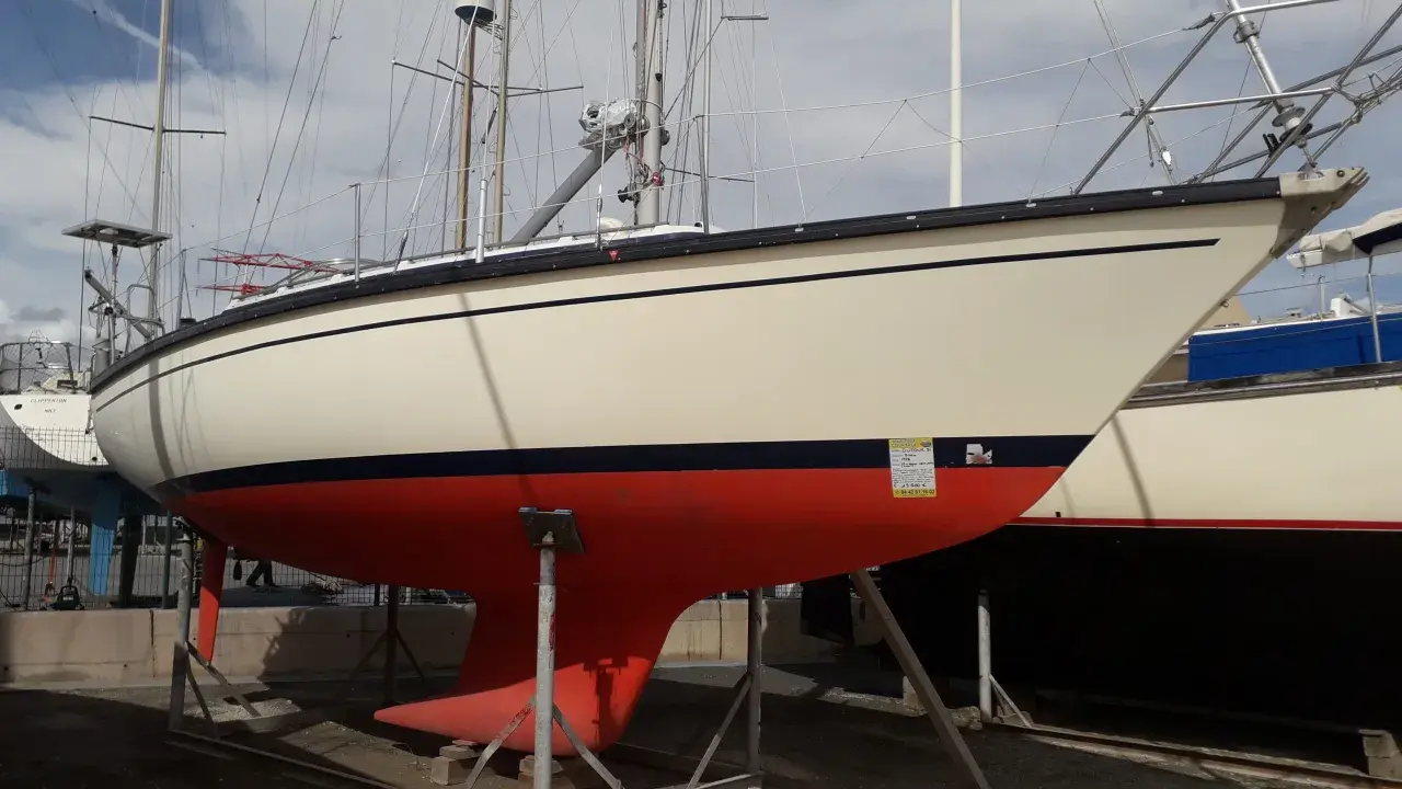 Voilier Dufour 31 sur bers. La coque est crème avec une bande bleue et une quille rouge vif.