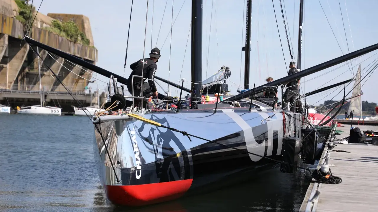 L'IMOCA Charal, un voilier de course futuriste, est amarré à quai. Des marins s'affairent sur le pont, préparant le navire pour une nouvelle aventure en mer.