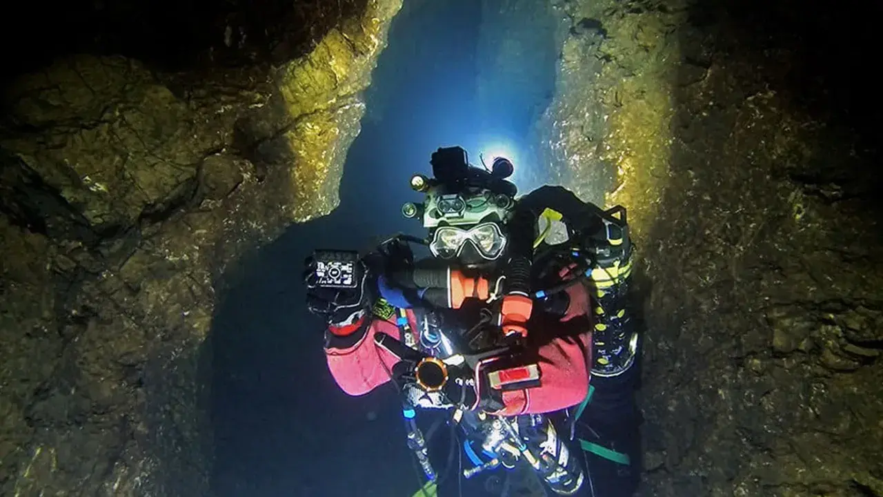 Plongée dans une grotte sous-marine, Xavier Meniscus filme les parois rocheuses éclairées par ses lampes.