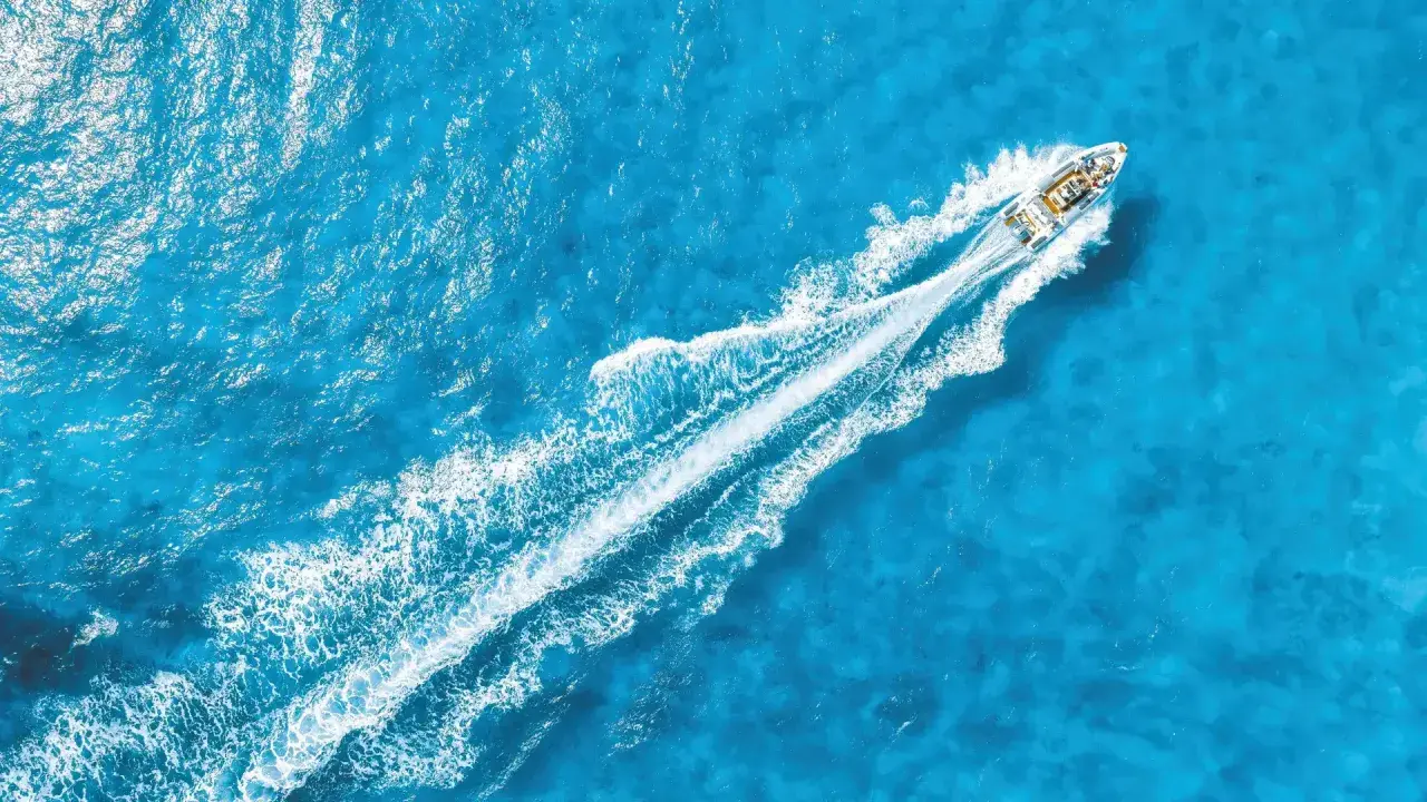 La coque d'un bateau fend les eaux bleues, laissant une traînée blanche de mousse.