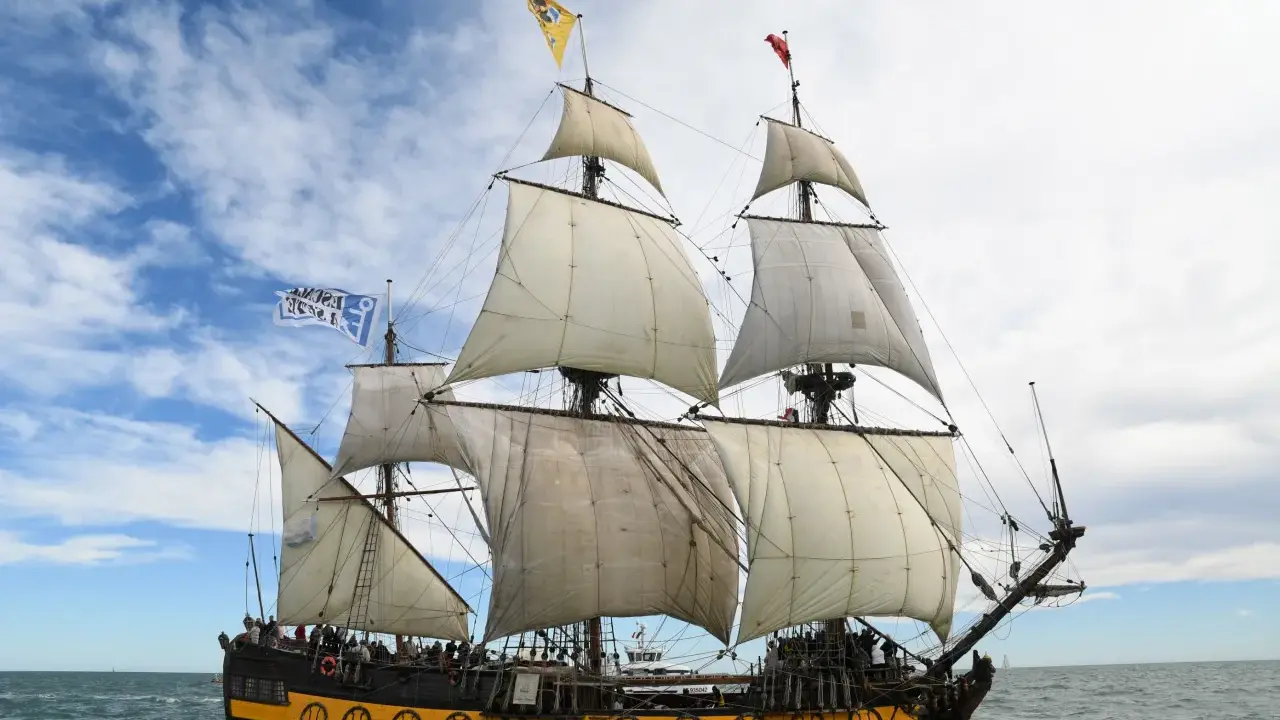 Le Shtandart, bateau historique aux voiles blanches, navigue sur une mer agitée sous un ciel nuageux.