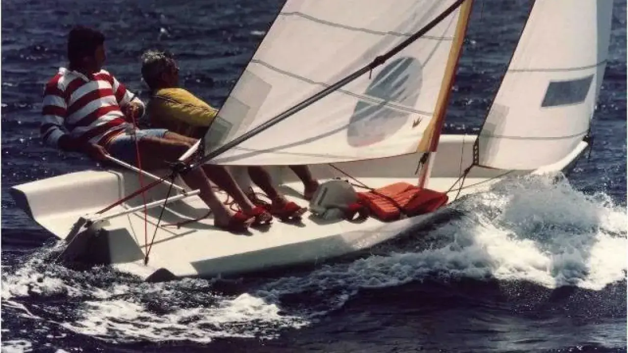 Deux personnes naviguent sur un dériveur Wizz, le bateau fend les vagues dans une joyeuse course.