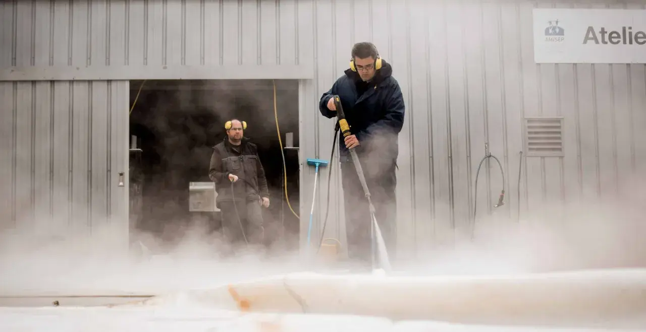 Deux hommes utilisent un nettoyeur haute pression pour nettoyer un voile de bateau avec du savon noir.