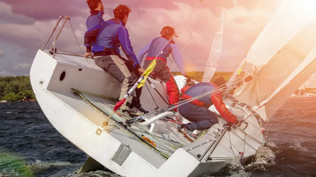 Équipe en pleine action pour apprendre la voile. Le voilier est incliné, les marins ajustent les voiles sous un ciel orageux.