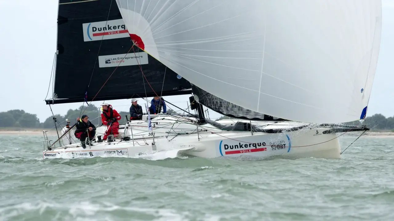 Un voilier "Dunkerque Voile" navigue avec un équipage concentré. Eliott Coville, peut-être à bord, profite de la course.