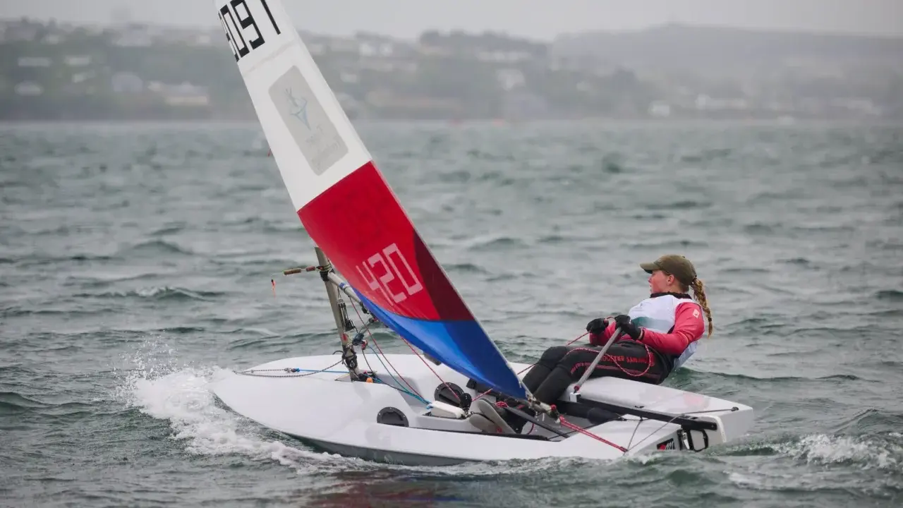Jeune navigatrice en dériveur **tabur 320**, voile rouge et bleue, naviguant sur une mer agitée.