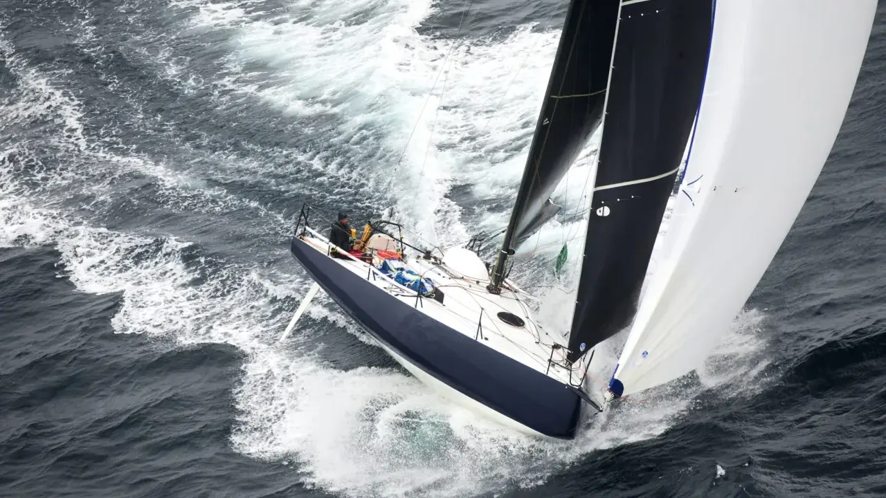 Un voilier de course fend les vagues, ses voiles noires et blanches gonflées par le vent. On dirait qu'il nous montre comment naissent les bateaux, prêts à conquérir l'océan.
