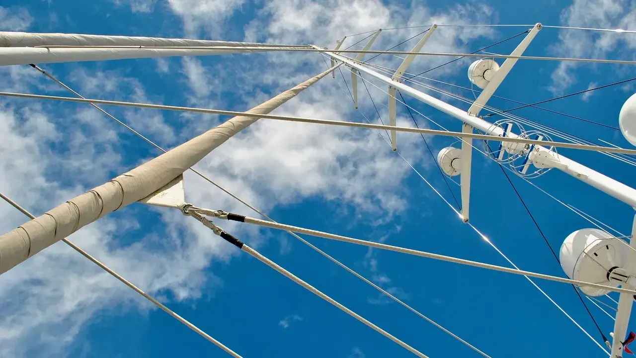 Vue plongeante sur le gréement d'un bateau, mâts blancs et cordages fins se découpant sur un ciel bleu et nuageux.