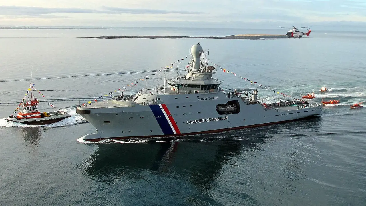 Un imposant bateau garde côte, le Landhelgisgæslan, navigue en mer, escorté par un remorqueur et suivi par des canots. Un hélicoptère survole la scène.