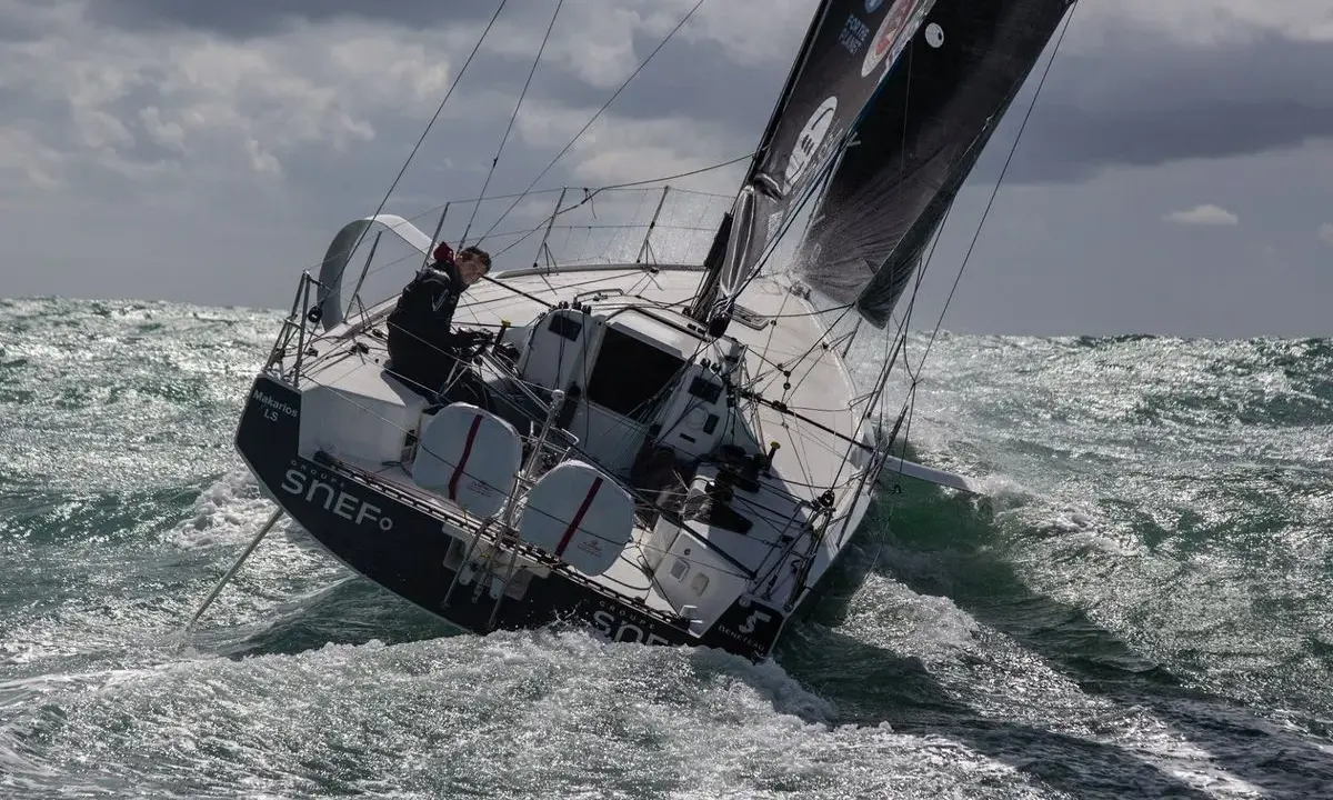 Xavier Macaire navigue sur un voilier dans une mer agitée, le bateau est incliné, les vagues déferlent.