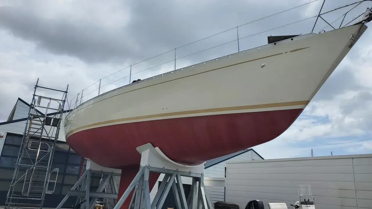 Le nouveau bateau de Jean Le Cam, un voilier blanc et rouge, est sur des supports à côté d'un atelier.