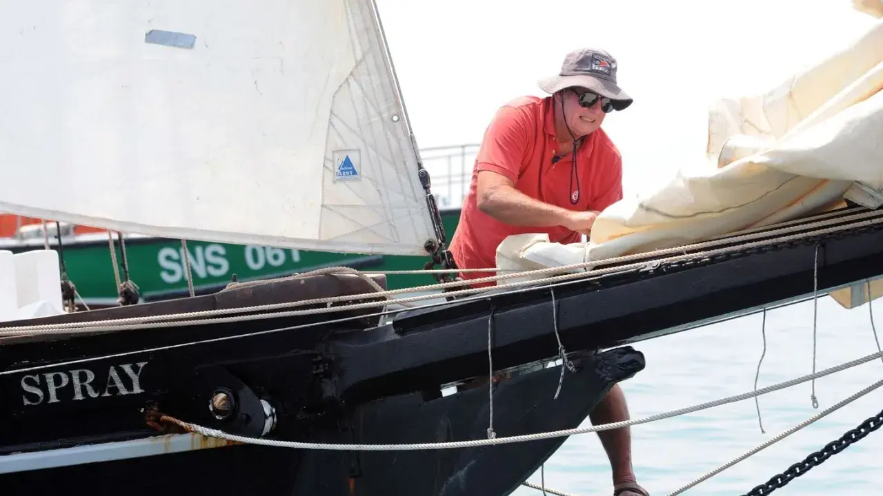 Un homme, Guy Bernardin, ajuste les voiles du Spray, un voilier historique, par une journée ensoleillée.
