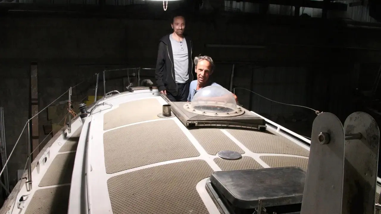 Nicole Van de Kerckhove et un autre homme sur le pont d'un voilier dans un hangar sombre.