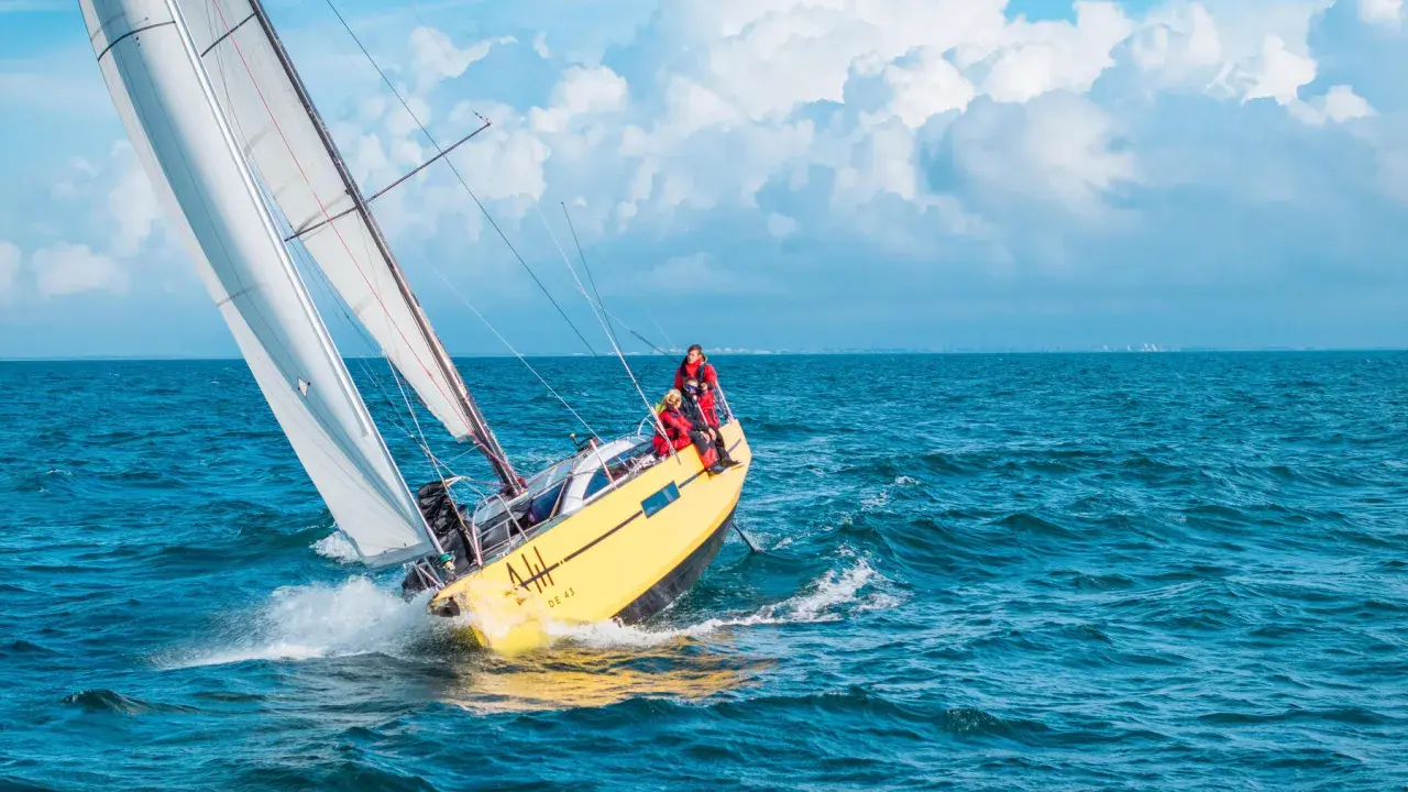 Un voilier jaune fend les vagues bleues, ses voiles blanches gonflées par le vent. L'équipage profite de cette belle journée pour faire la voile.