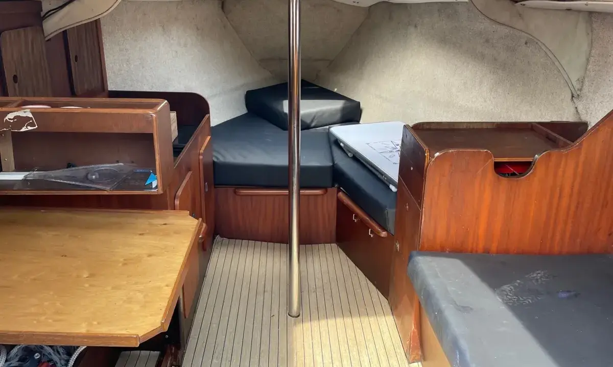 L'intérieur du Jeanneau Brio offre un espace de vie confortable avec des banquettes en tissu noir, une table en bois et des boiseries chaleureuses.