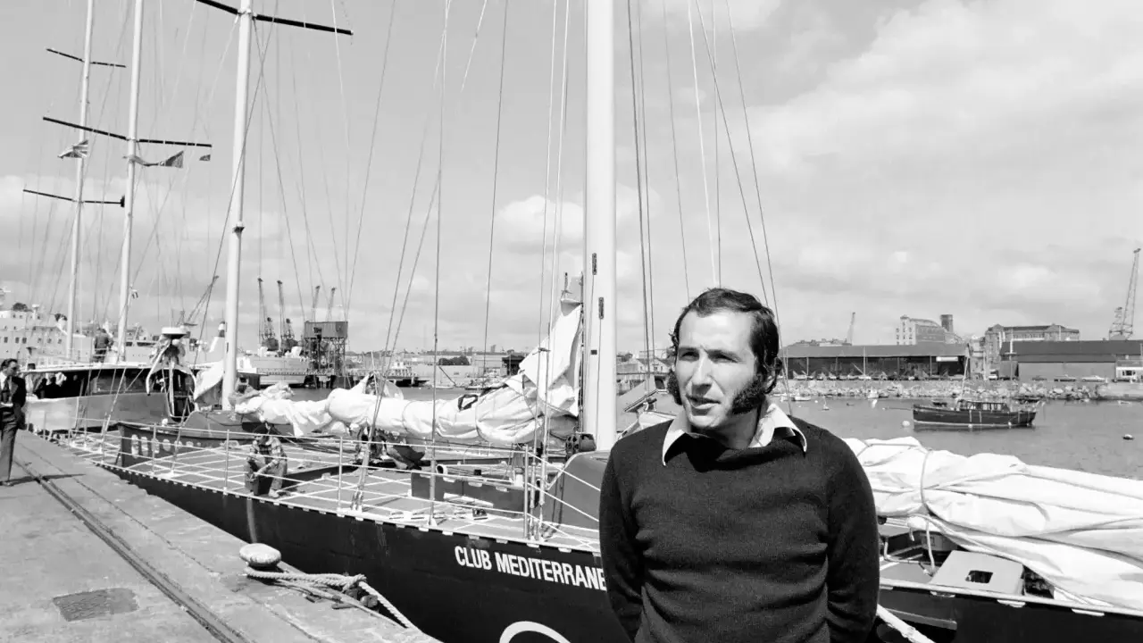 Un homme pose devant le voilier "Club Mediterranee". Ce navigateur célèbre semble prêt pour une nouvelle aventure maritime.