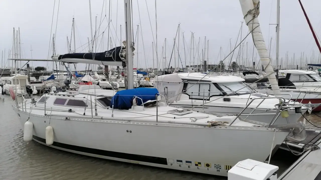 Un voilier blanc, "PEELIN", est amarré dans un chantier naval. D'autres bateaux sont visibles en arrière-plan.