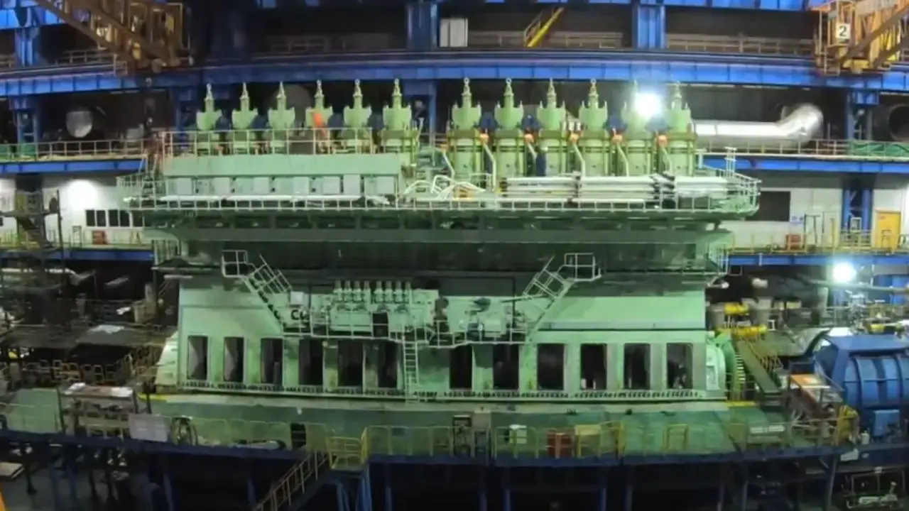 Un immense moteur vert, prêt à propulser un porte-conteneurs, se dresse dans un atelier de construction navale.