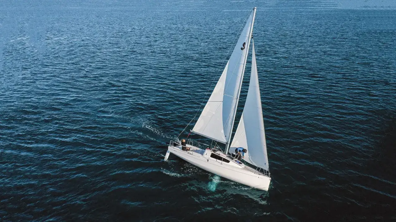 Un voilier blanc navigue sur une mer bleue. Sa quille est visible sous l'eau, stabilisant le bateau.