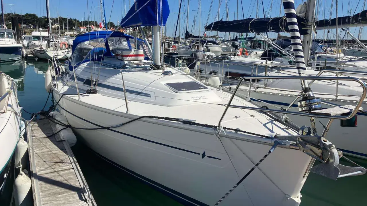 Bavaria 32, un voilier blanc avec une voile bleue, amarré dans un port. Avis sur ce modèle de bateau.