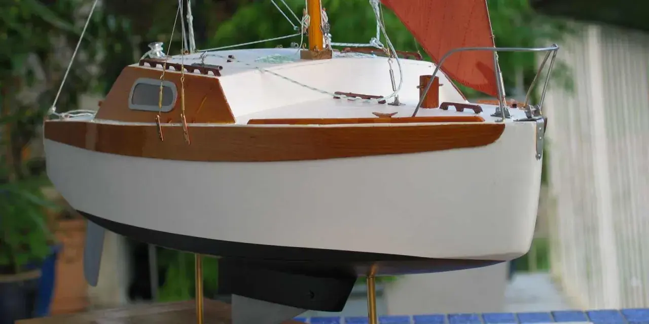Modèle de voilier corsaire, coque blanche et bois verni, voile orange. Fiche technique détaillée.