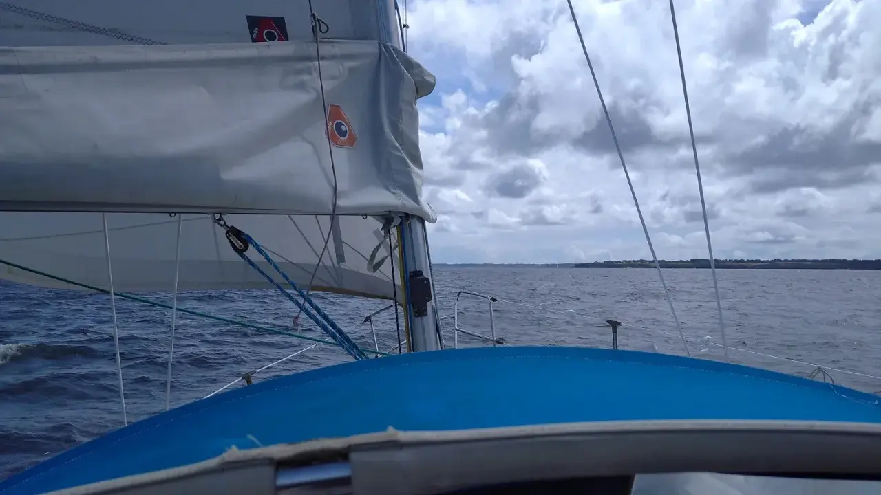 Vue depuis un voilier, avec la liste des voiles d'un bateau gonflées par le vent. La mer est agitée sous un ciel nuageux.