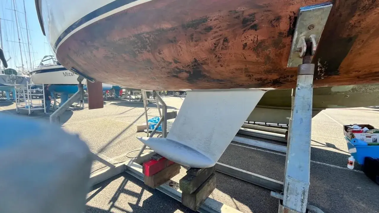 Vue du dessous d'un voilier sur bers. Le safran est visible, prêt pour l'étape 22 de la fiche technique.