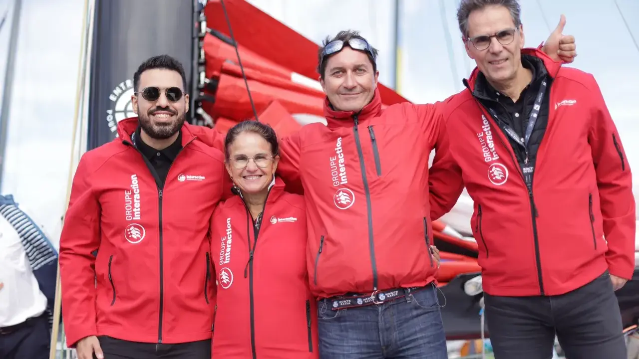 Erwan Thiboumery et trois autres personnes souriantes portent des vestes rouges du Groupe Interaction, devant un bateau.