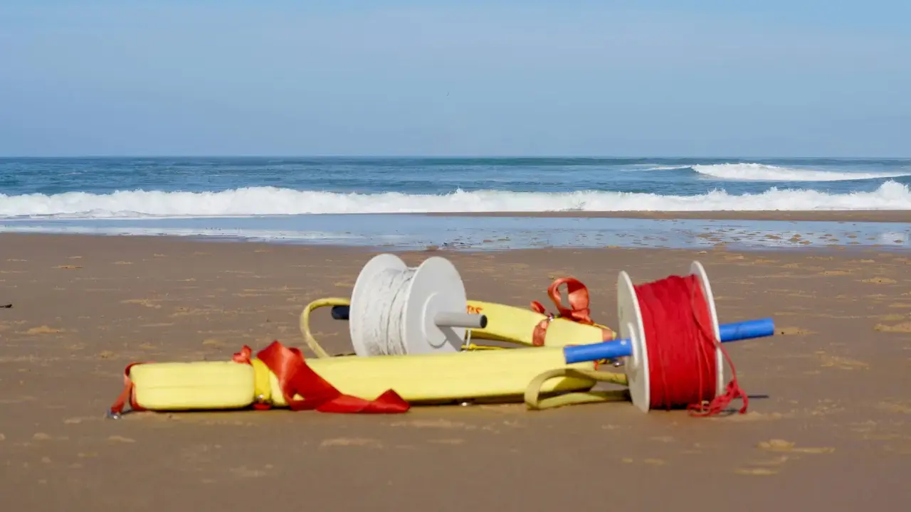 Deux bobines de fil, une blanche et une rouge, sont attachées à un tube de sauvetage jaune sur une plage.