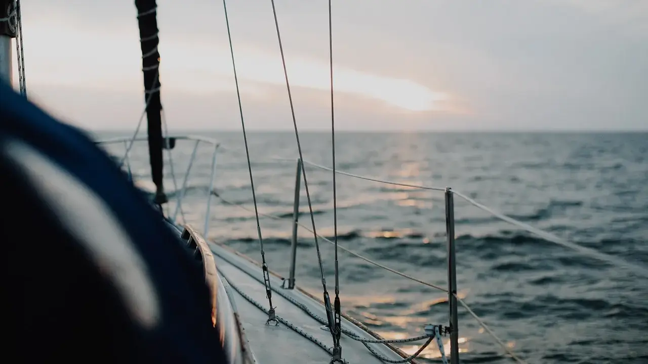 Vue depuis le pont d'un voilier insubmersible naviguant sur une mer calme au coucher du soleil.