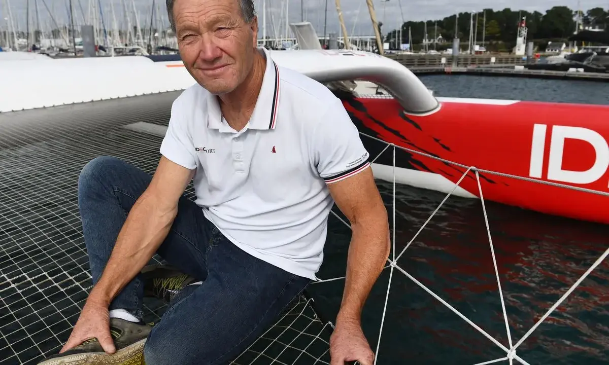 Francis Joyon, marin légendaire, pose sur le filet d'un trimaran rouge vif, prêt pour une nouvelle aventure en mer.