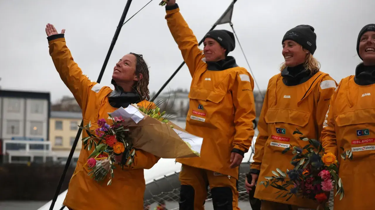Des femmes en cirés jaunes célèbrent la fin du célèbre projet, bouquets à la main.