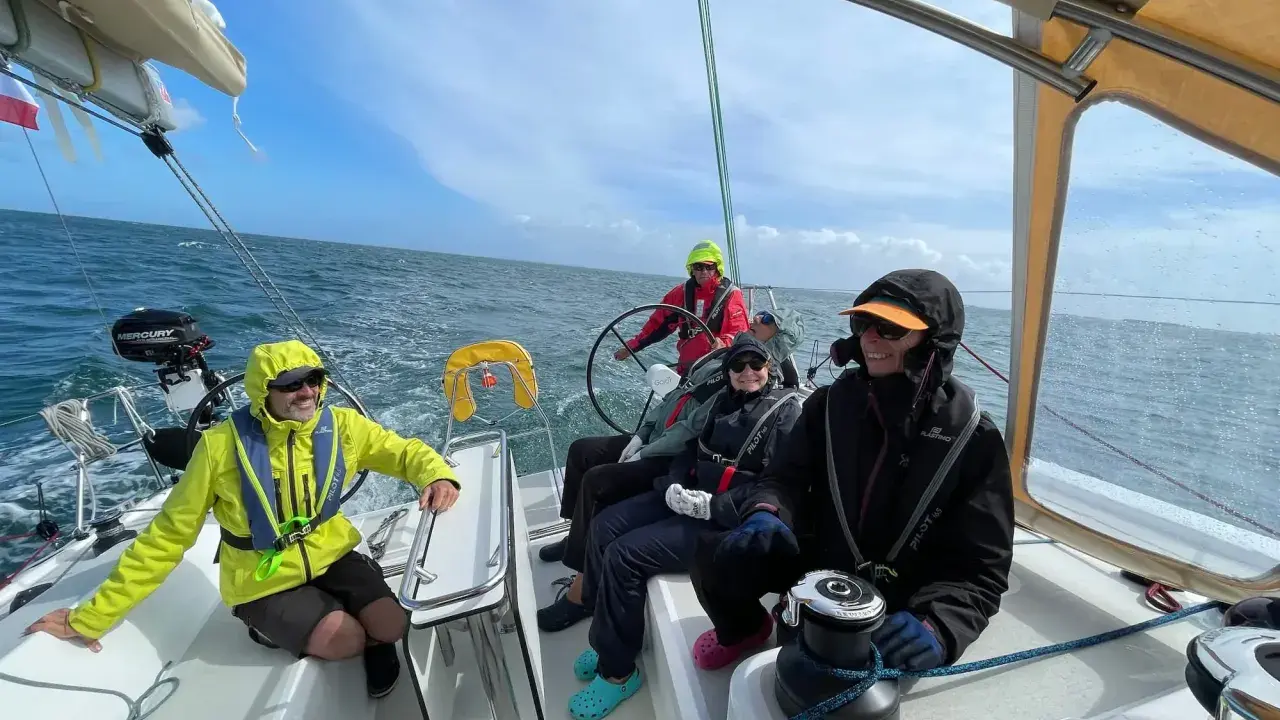Équipage souriant sur un voilier, profitant de la navigation. Personne n'a besoin d'écoper, la mer est calme.