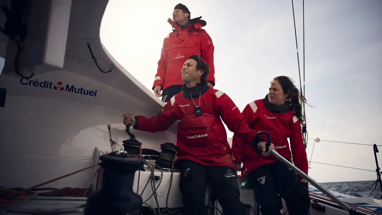 Amélie Grassi et son équipage en pleine action sur un voilier Crédit Mutuel. Le vent souffle, la mer est agitée.