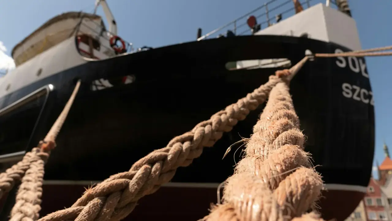 Gros plan sur des cordages épais assurant l'amarrage d'un bateau noir et blanc, avec des bâtiments colorés en arrière-plan.