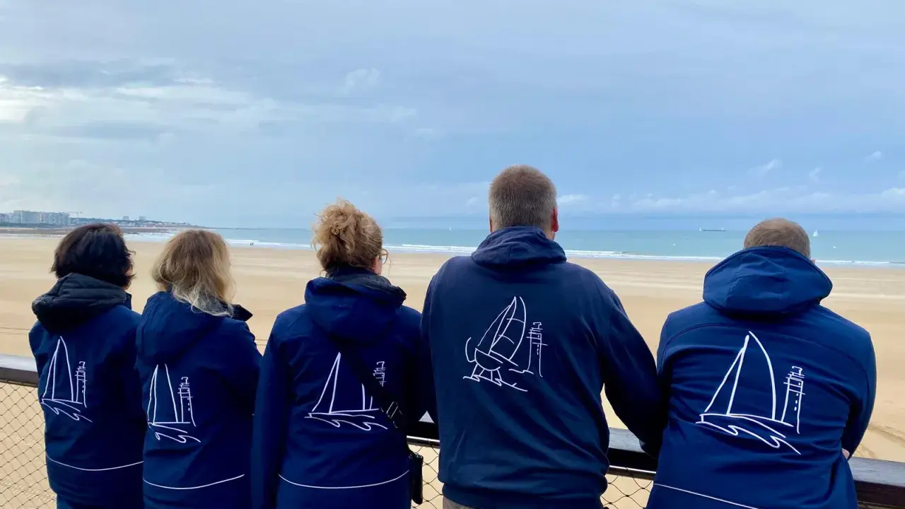 Cinq personnes portent des vestes bleues avec des voiliers dessinés. Benoit Marie et ses amis admirent la mer.