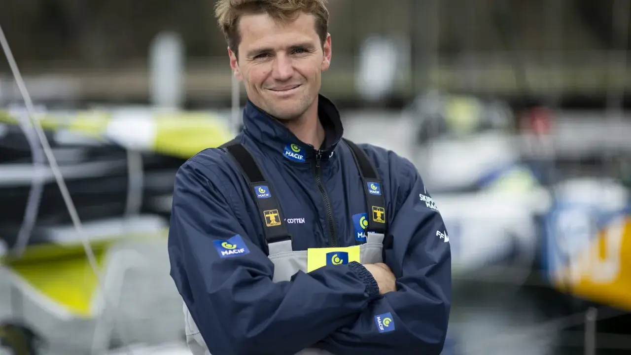 L'athlète marin Lois Berrehar, souriant, porte une veste bleue MACIF avec des logos. Derrière lui, des voiliers colorés.