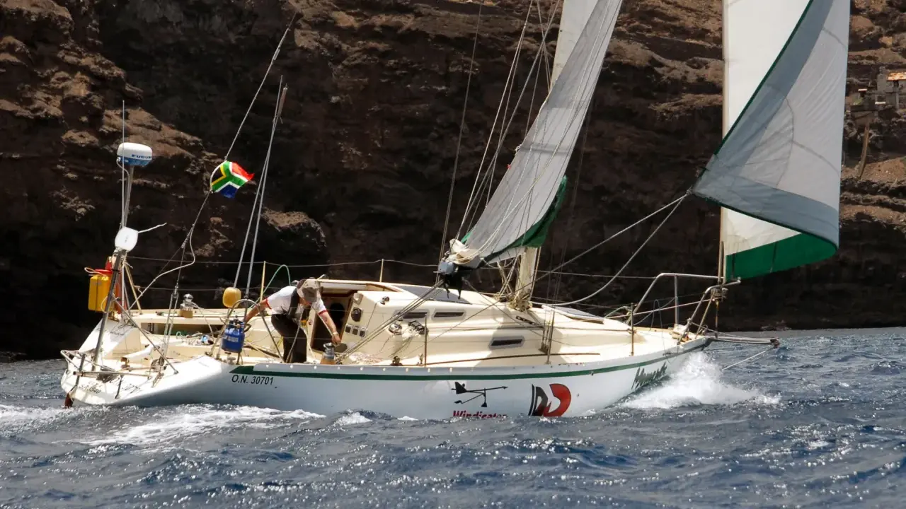 Un voilier cap horn, le "Windicator", navigue près d'une côte rocheuse. Le drapeau sud-africain flotte fièrement.