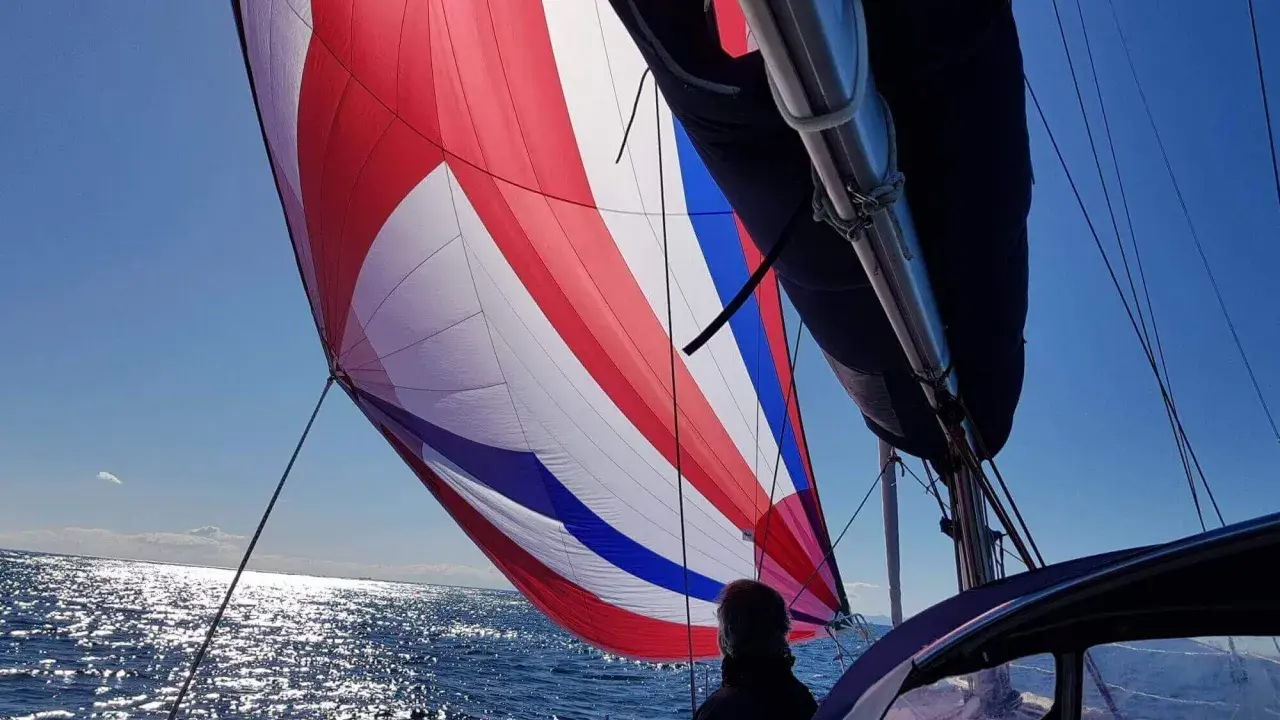 Un spi symétrique aux couleurs vives gonflé par le vent, naviguant sur une mer scintillante sous un ciel bleu clair.