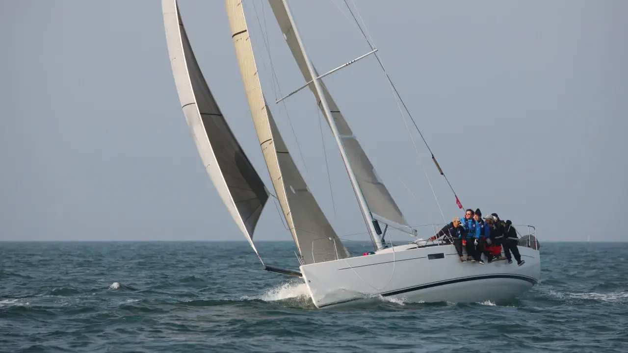 Équipage sur un voilier blanc, le foc et le génois gonflés par le vent, naviguant sur une mer agitée.