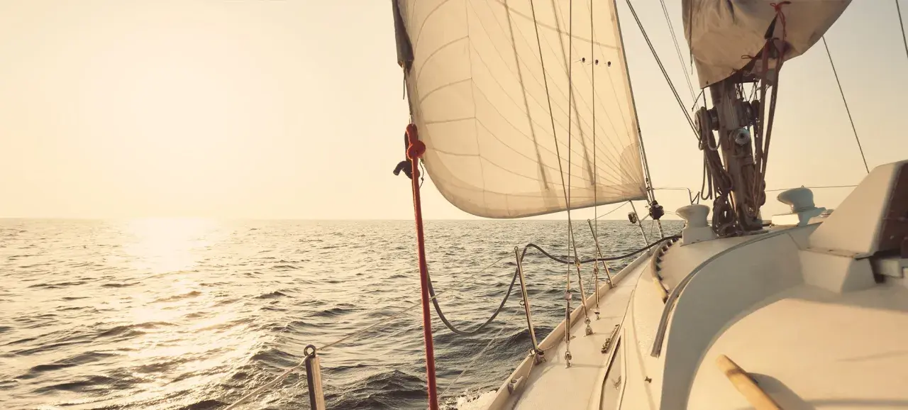 Voile de bateau gonflée par le vent, naviguant sur une mer calme au coucher du soleil.