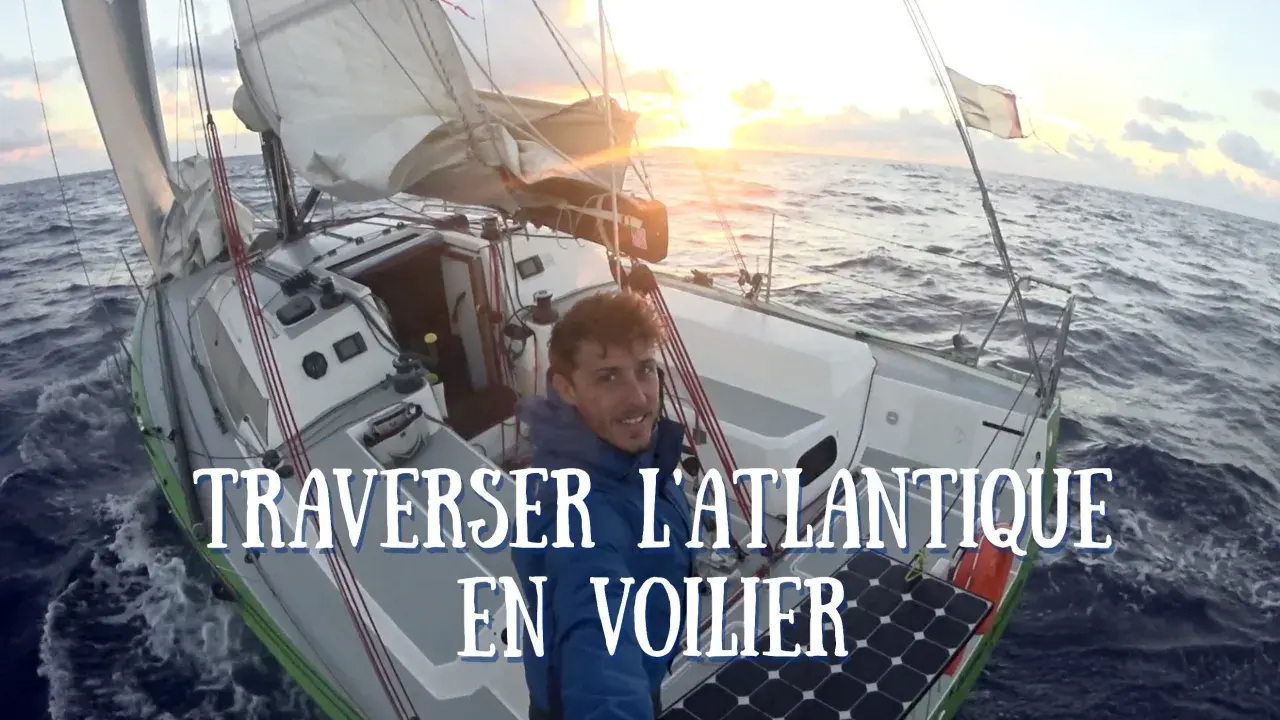 Un homme souriant sur un voilier en pleine traversée de l'Atlantique. Le soleil se lève, illuminant les voiles. Quel voilier pour traverser l'Atlantique ? Celui-ci semble parfait.